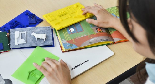 Criança lendo um livro tátil graças à acessebilidade na impressão 3D
