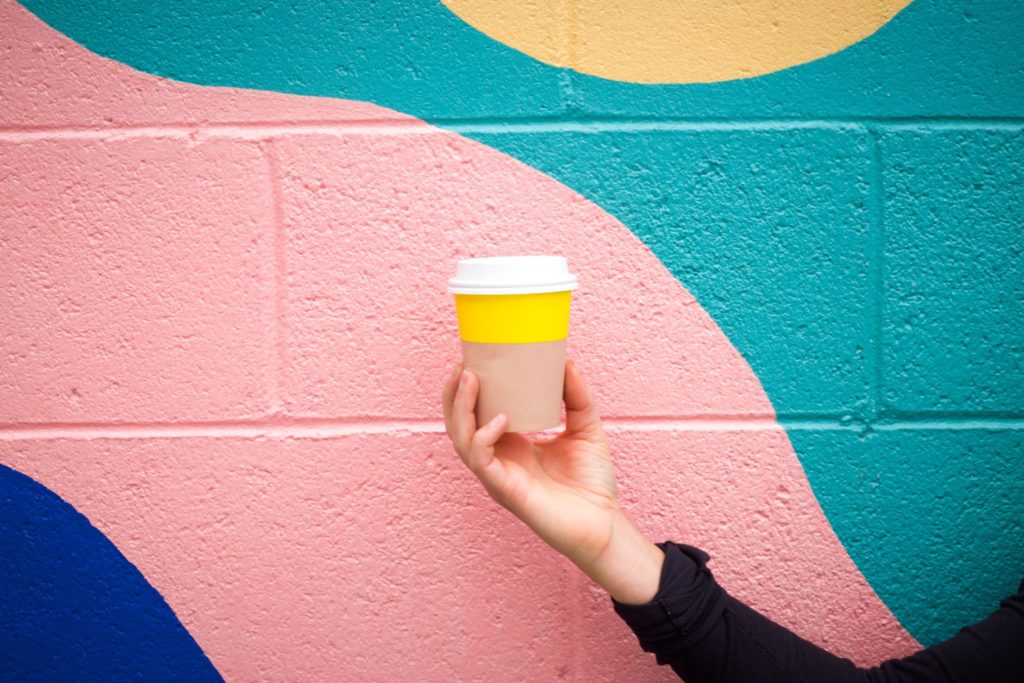 pessoa segurando um copo de café na frente de um muro colorido, aplicando o design thinking