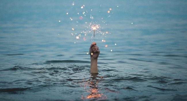mão segurando uma vela com faísca submersa no mar como forma de dizer que ainda é possivel inovar na sua empresa