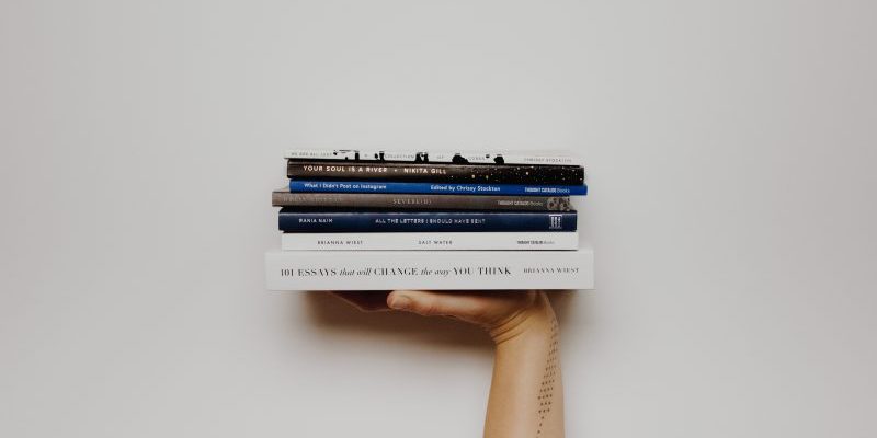 livros de criatividade e design pessoa segurando cinco livros empilhados com uma mão